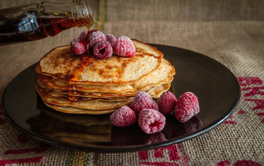 Stack of pancakes topped with raspberries and syrup on a dark plate.